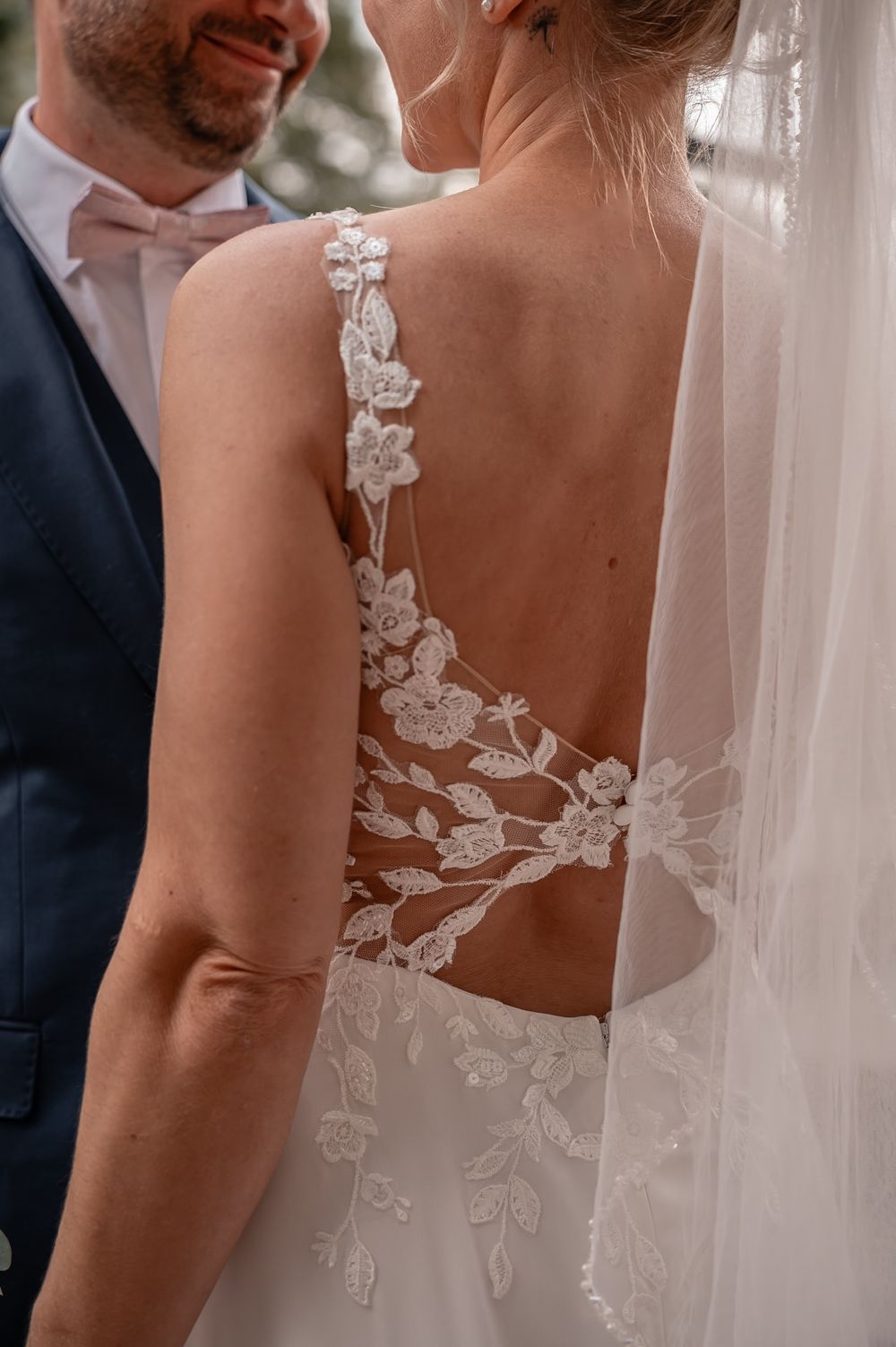 Close-up detail of a wedding dress showing delicate white lace appliques on sheer fabric with veil.