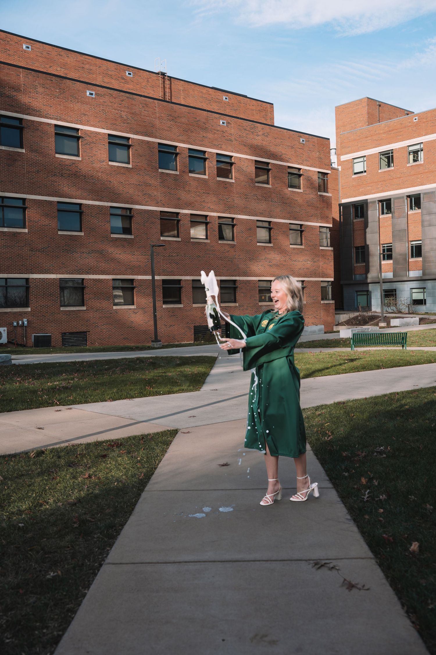Graduate in green cap and gown walking along brick campus path at George Mason University | Northern Virginia senior portraits.