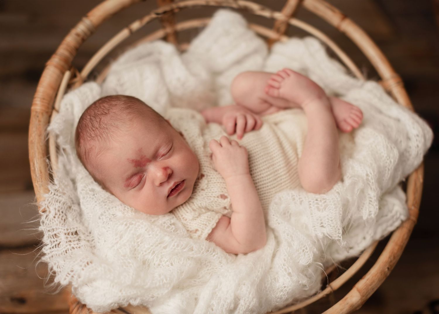 Sleeping newborn baby wrapped in delicate white lace rests peacefully in a wooden basket.