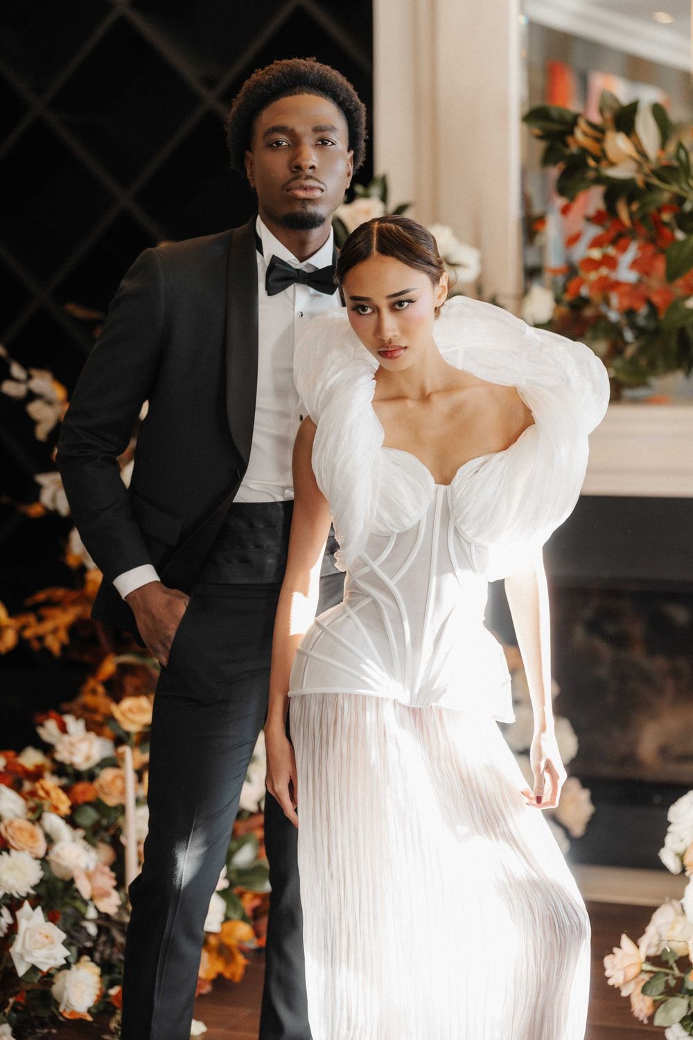 A bride in a white wedding dress poses elegantly against a backdrop of floral arrangements.
