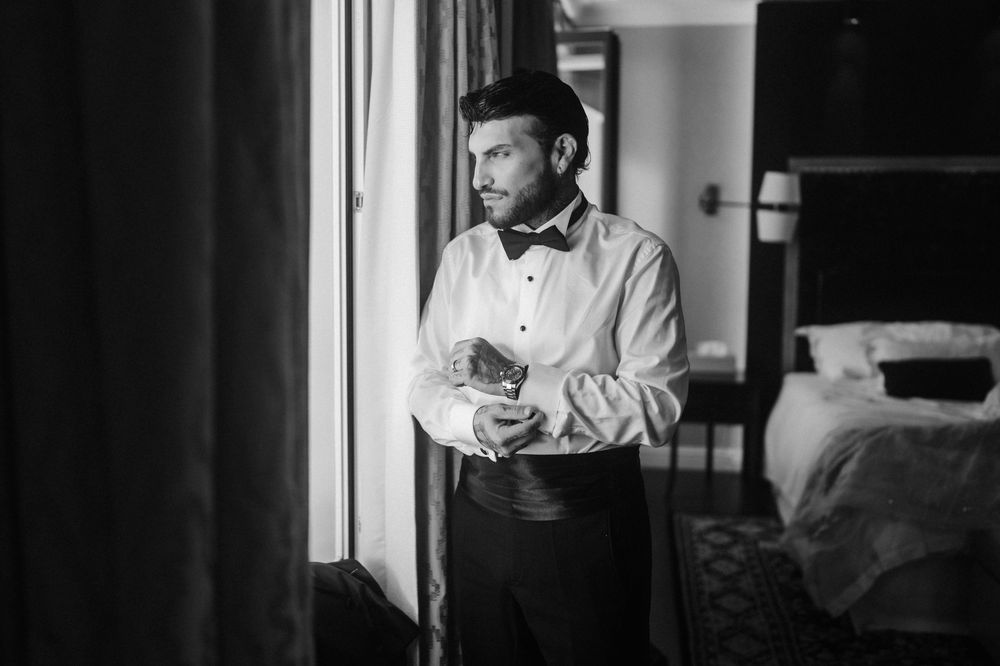 Person in business attire looking at smartphone while standing near office window in black and white photo.