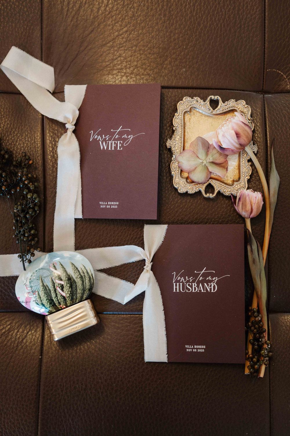 Wedding vow books for husband and wife with white ribbons and dried flowers on brown leather surface.