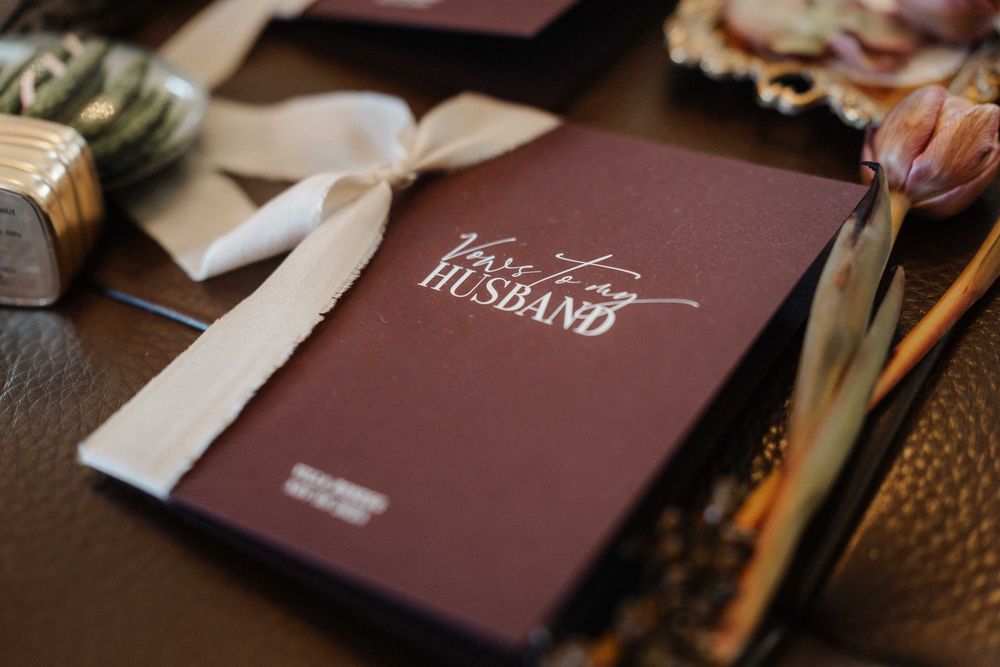 Wedding invitations in burgundy folders arranged on a wooden surface.
