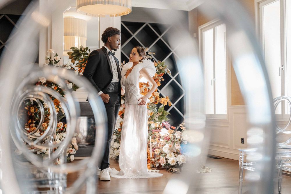 A romantic wedding couple embraces in an elegant white room with decorative mirrors and soft lighting.
