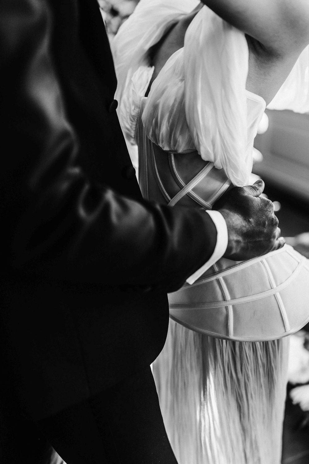 Black and white photo series showing a woman in a white dress being laced up in a traditional corset.