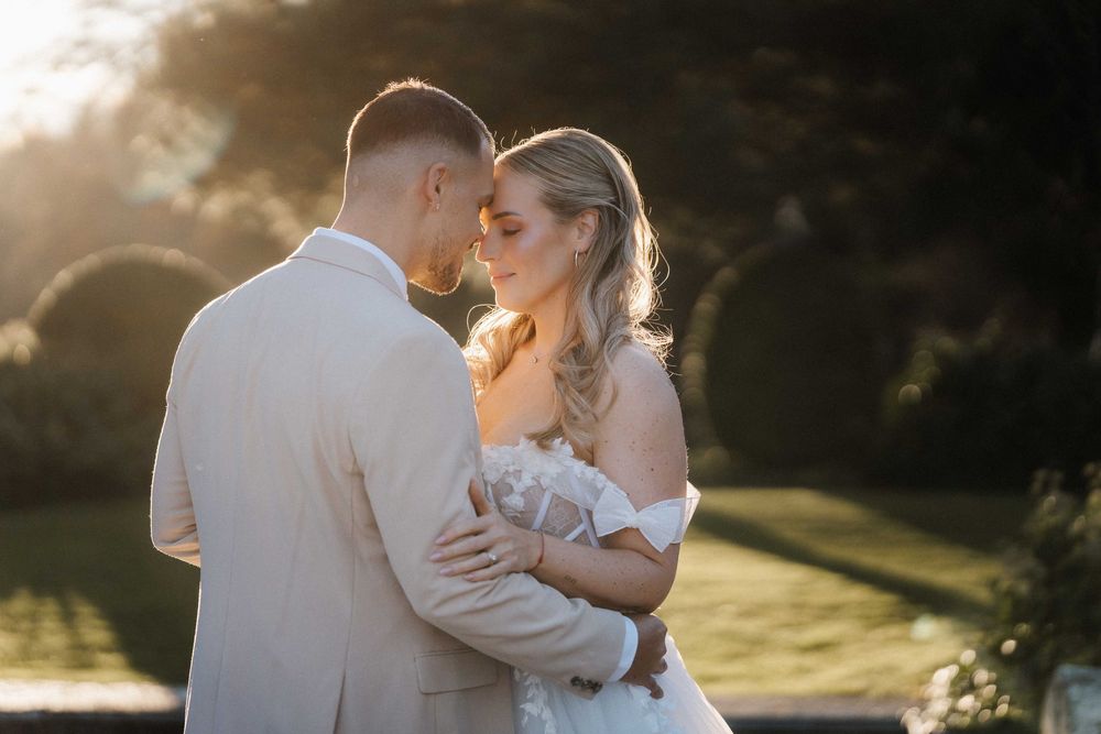 A romantic sunset wedding portrait with soft golden light filtering through trees.