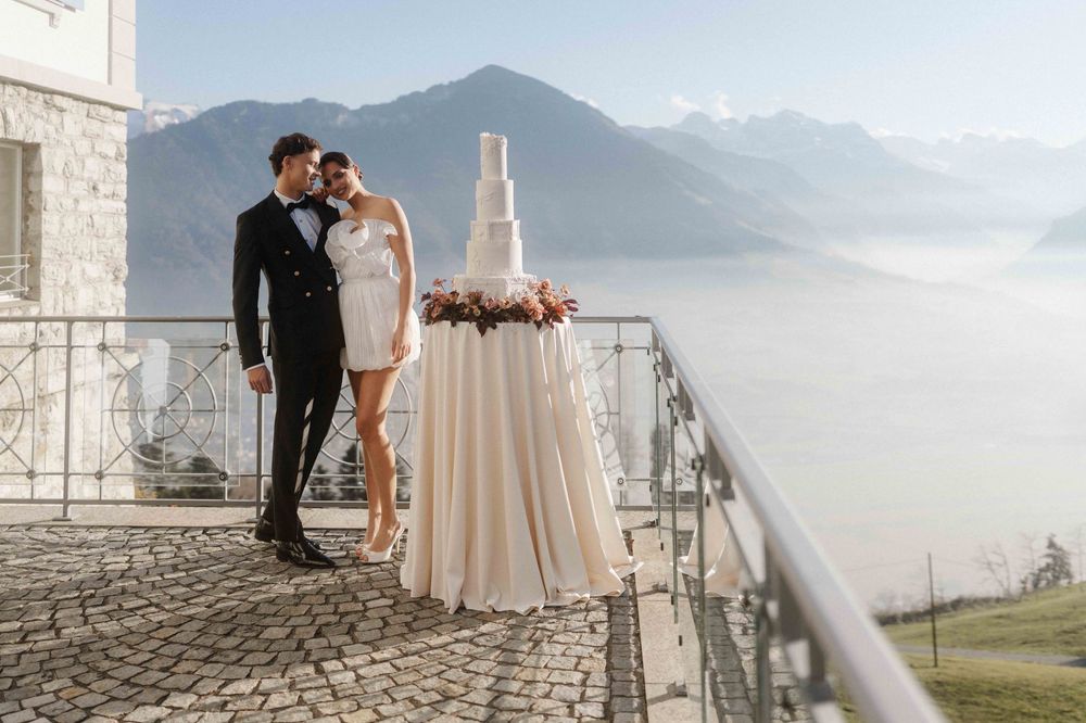 A romantic couple shares a tender moment on a balcony overlooking a scenic mountain landscape at sunset.