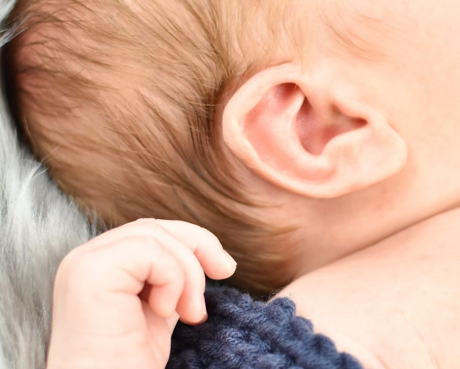Close-up detail of a newborn baby's ear and tiny hand against soft fabric.