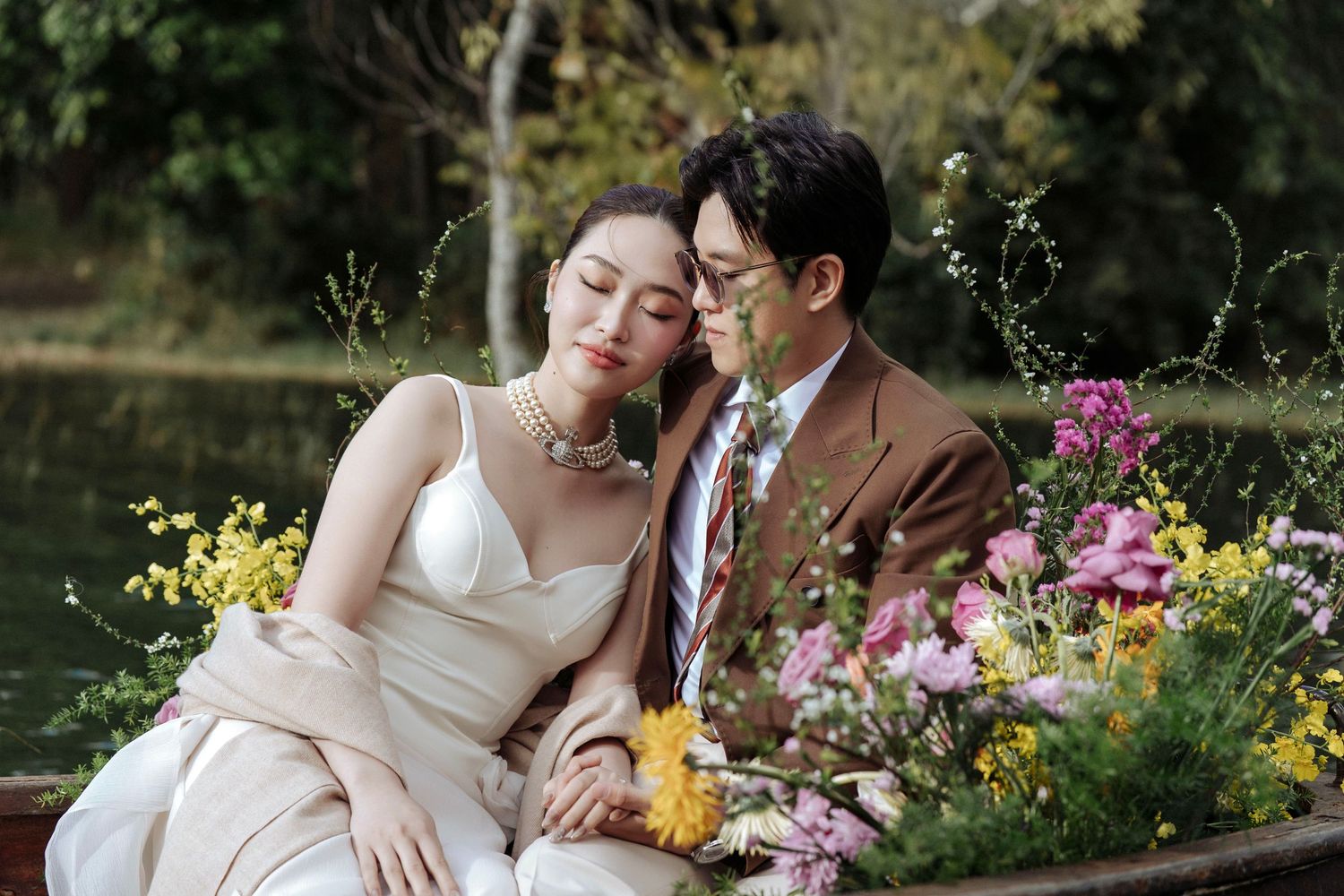 Romantic bride and groom in a flower-adorned boat, sharing a tender moment surrounded by colorful blooms.