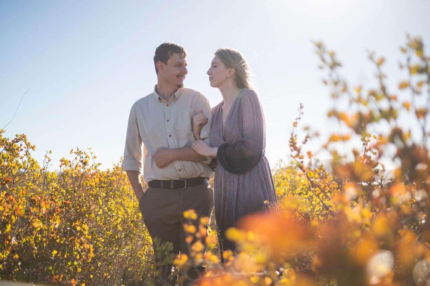 Romantic couple in flower field at golden hour sunset with sunlight glowing through yellow wildflowers.