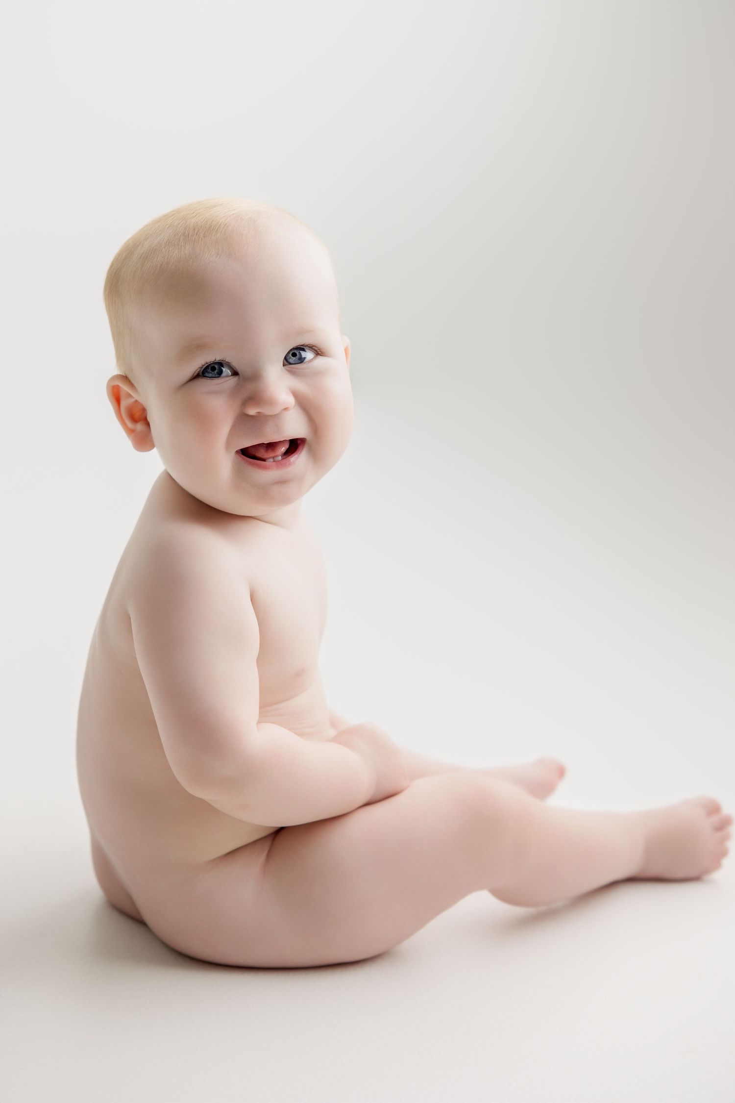 A happy baby sitting on a white background showing joyful expression.