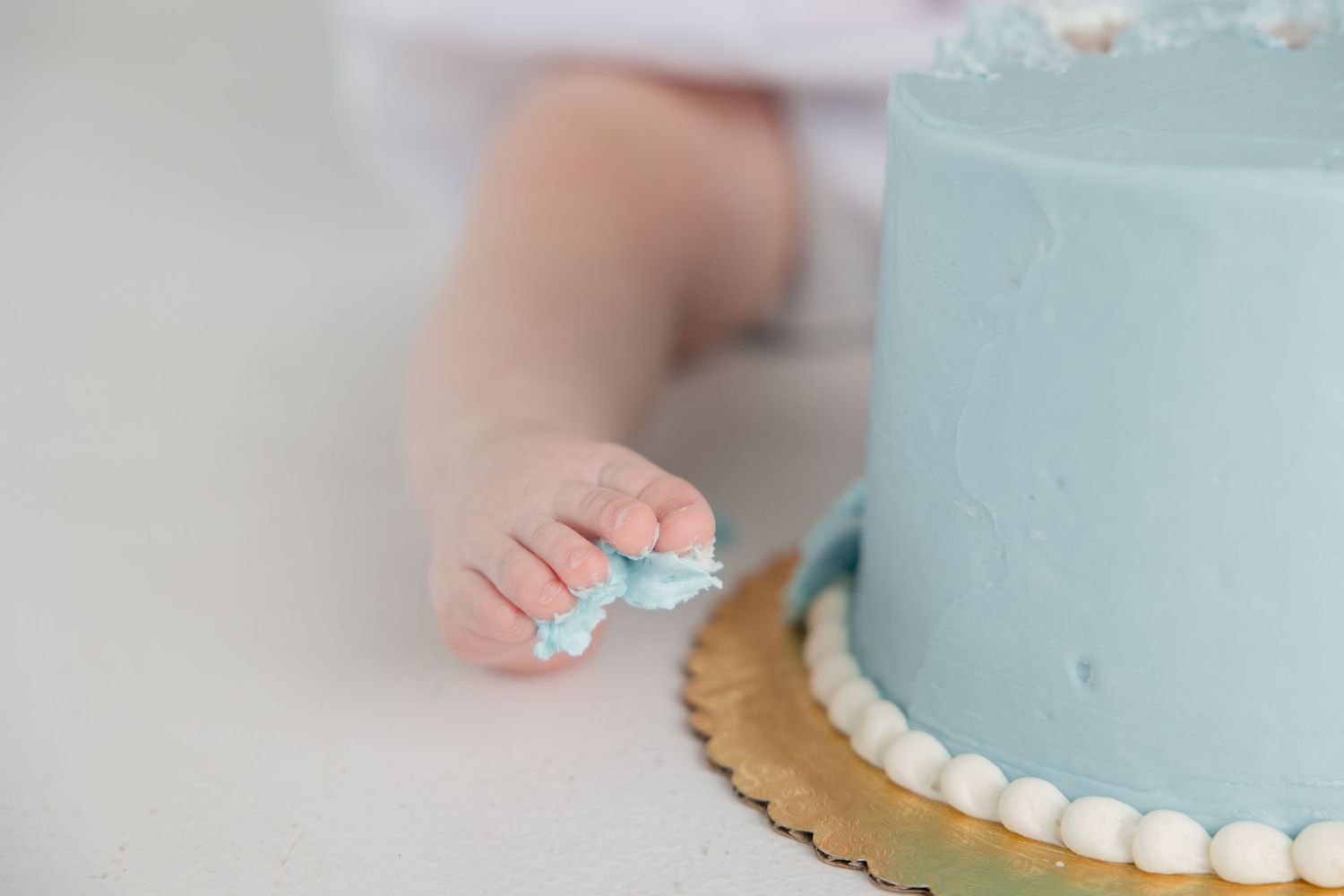 Light blue birthday cake decorated with white pearls and gold accents on white surface.