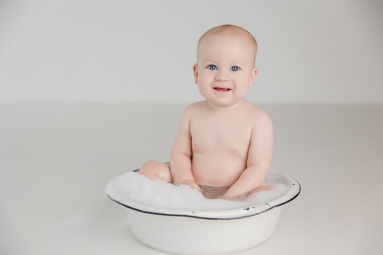 Baby sitting on white cushion during minimalist photography session.