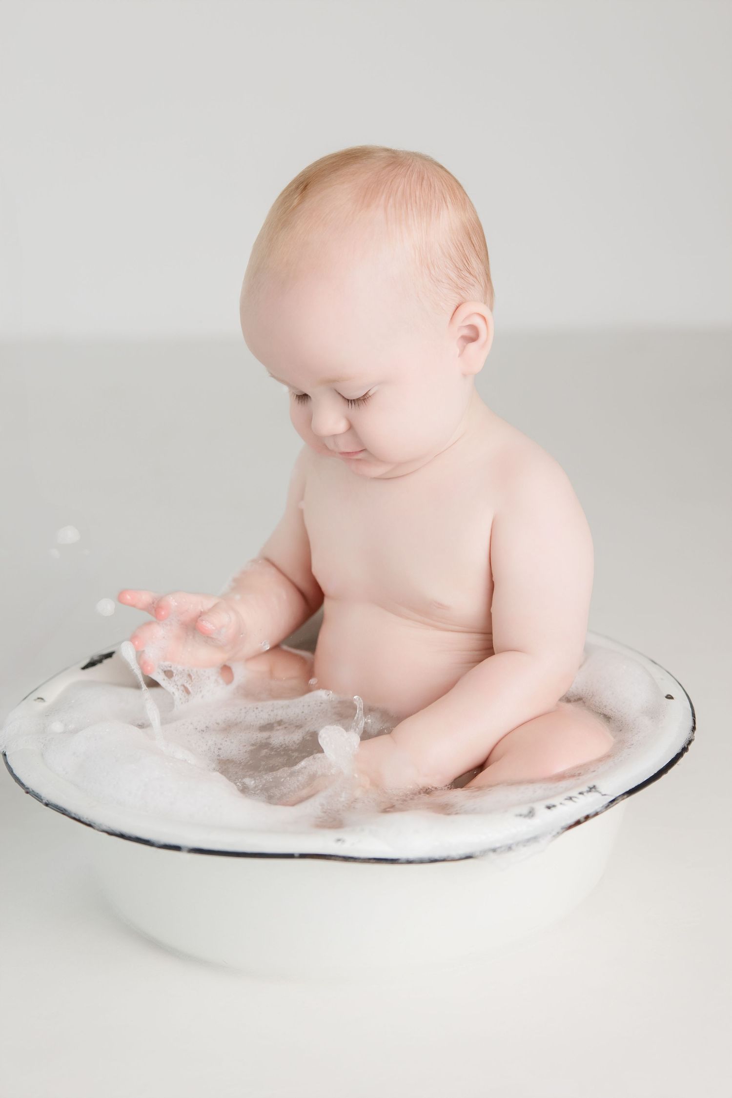 Baby sitting in white enamel basin during simple studio photography session.