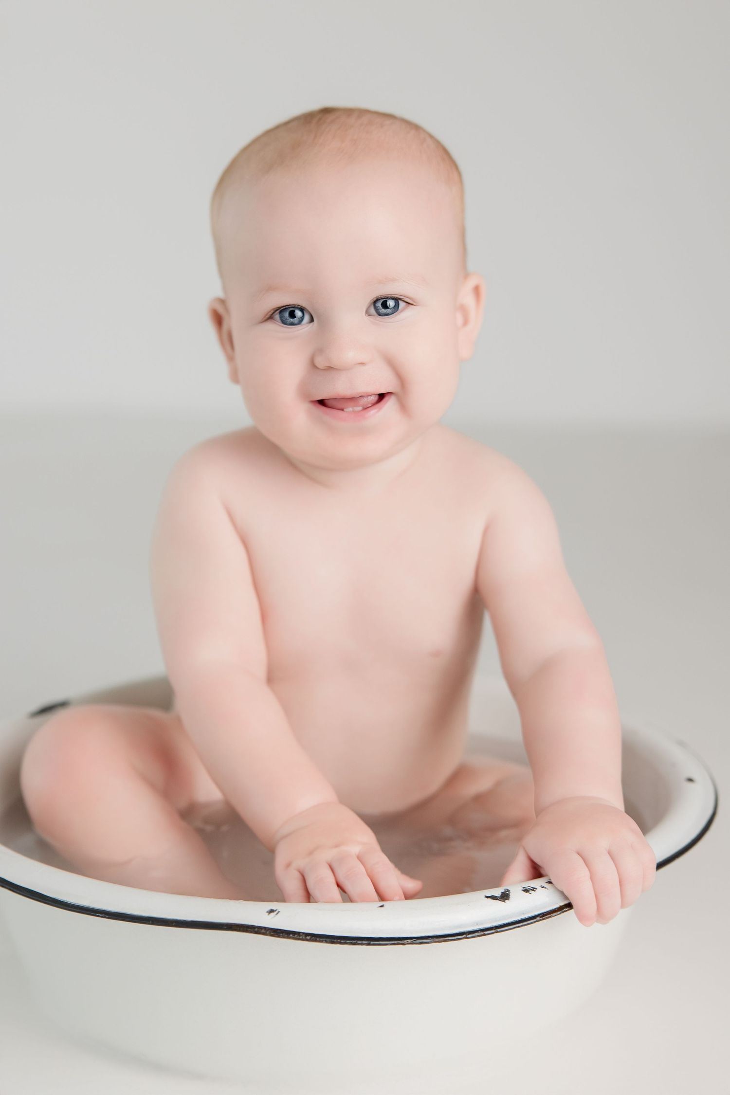 Smiling baby lying on white curved surface during minimalist photo session.
