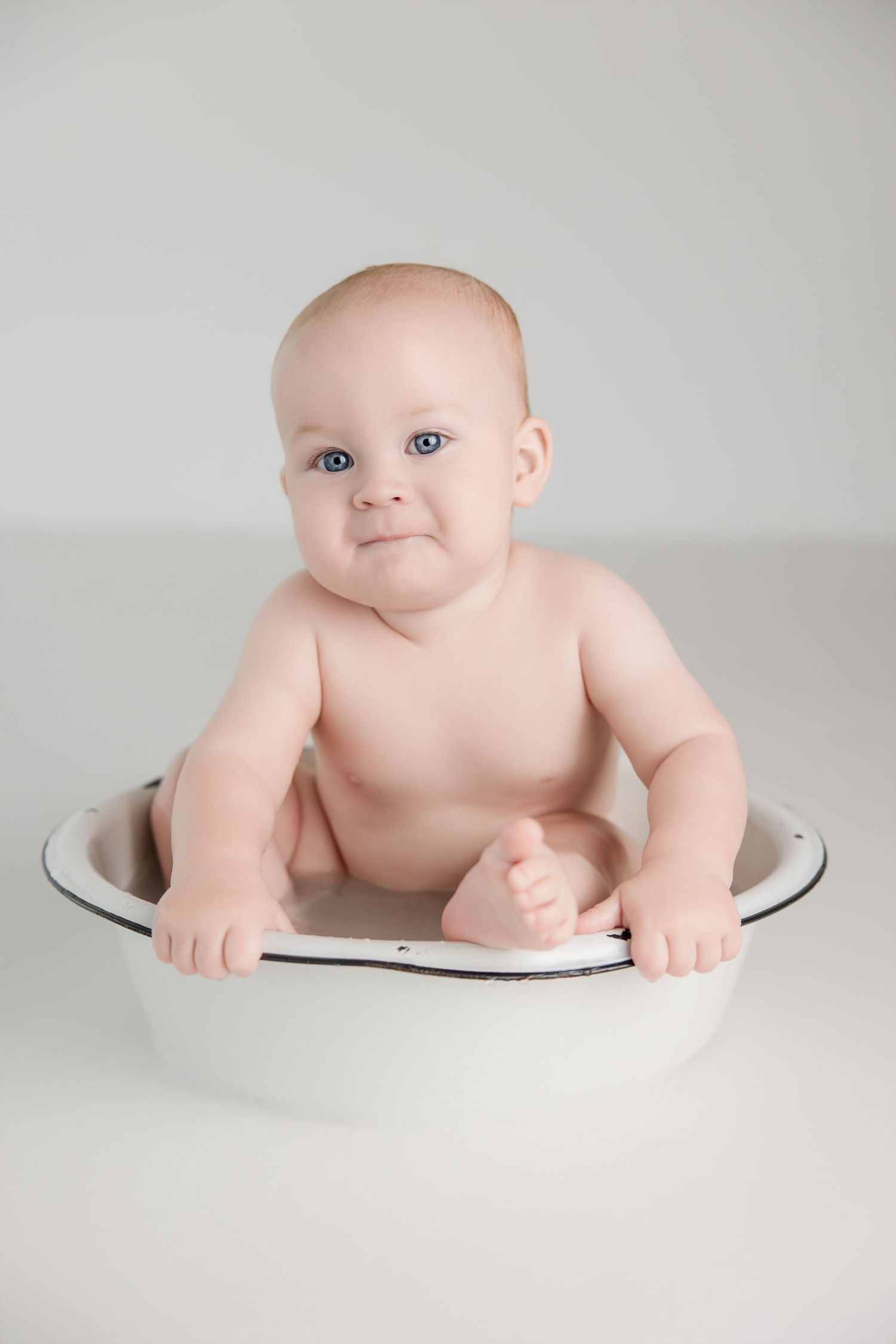 Baby laying on white surface in artistic studio portrait session with minimalist backdrop.