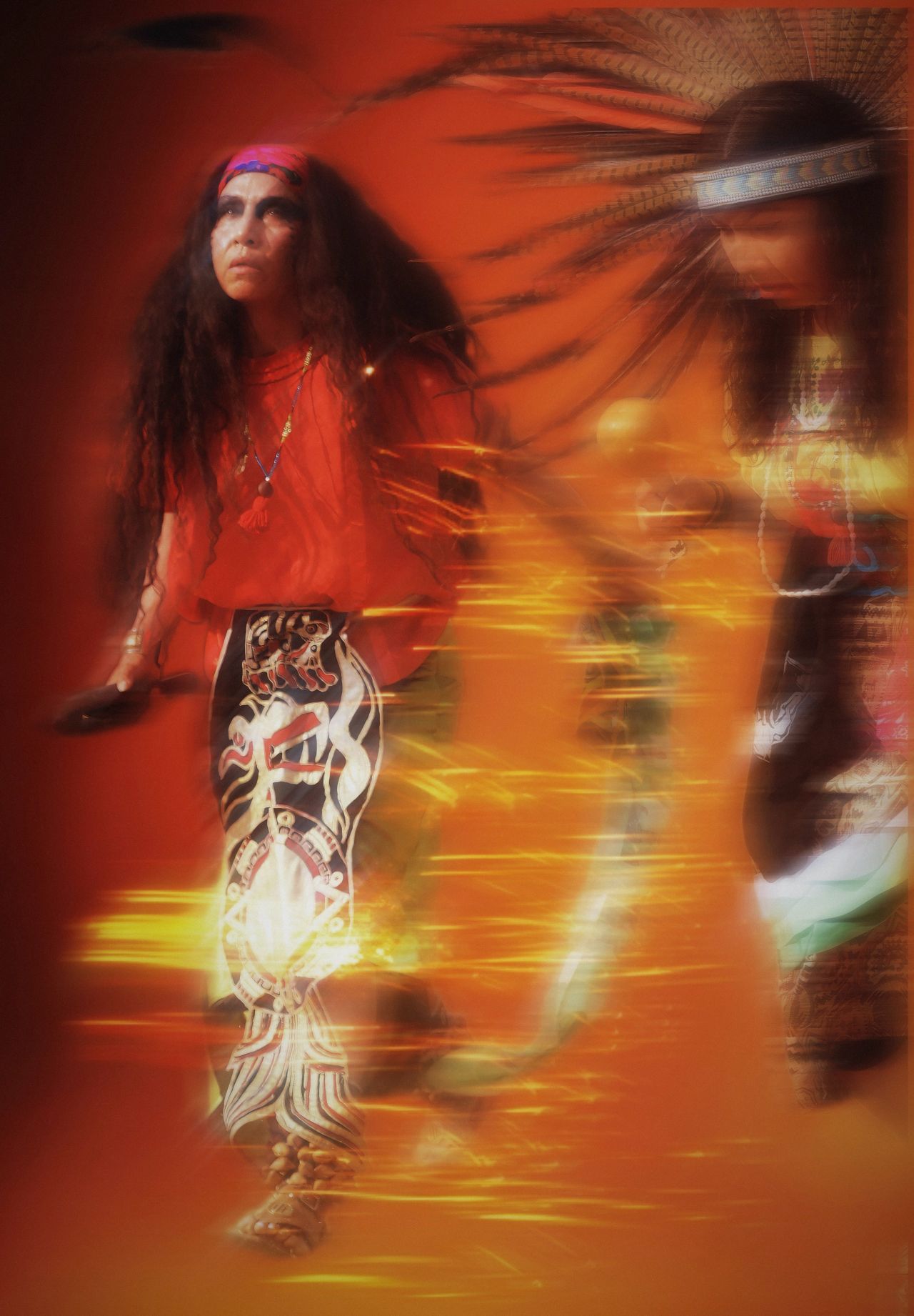 Motion-blurred performance of traditional Native American dance with orange and red lighting effects.