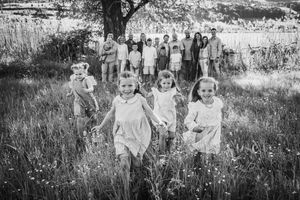 People gathering outdoors in a grassy field wearing vintage clothing in what appears to be a historic photograph.