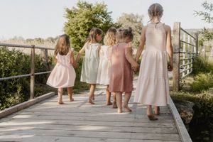 Line of bridesmaids in pink dresses posing while walking down an outdoor garden pathway at sunset.