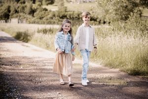 A couple holding hands walks along a winding dirt path through a meadow in warm natural lighting.