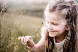 A person smiles while sitting in a golden field of tall grass during a sunny afternoon.