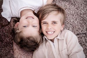 Two children laying on grey carpet and smiling together, one upside down.