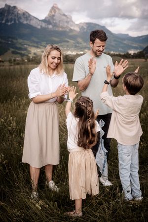 A family wearing neutral tones shares joyful moments together in a mountain meadow at sunset.