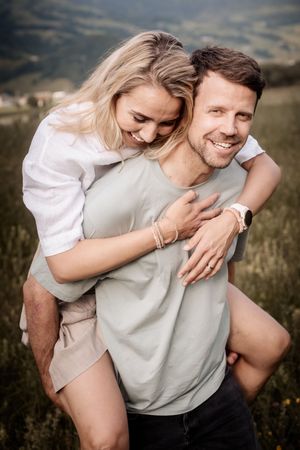 A couple in casual attire shares playful and intimate moments together in a grassy outdoor setting at sunset.