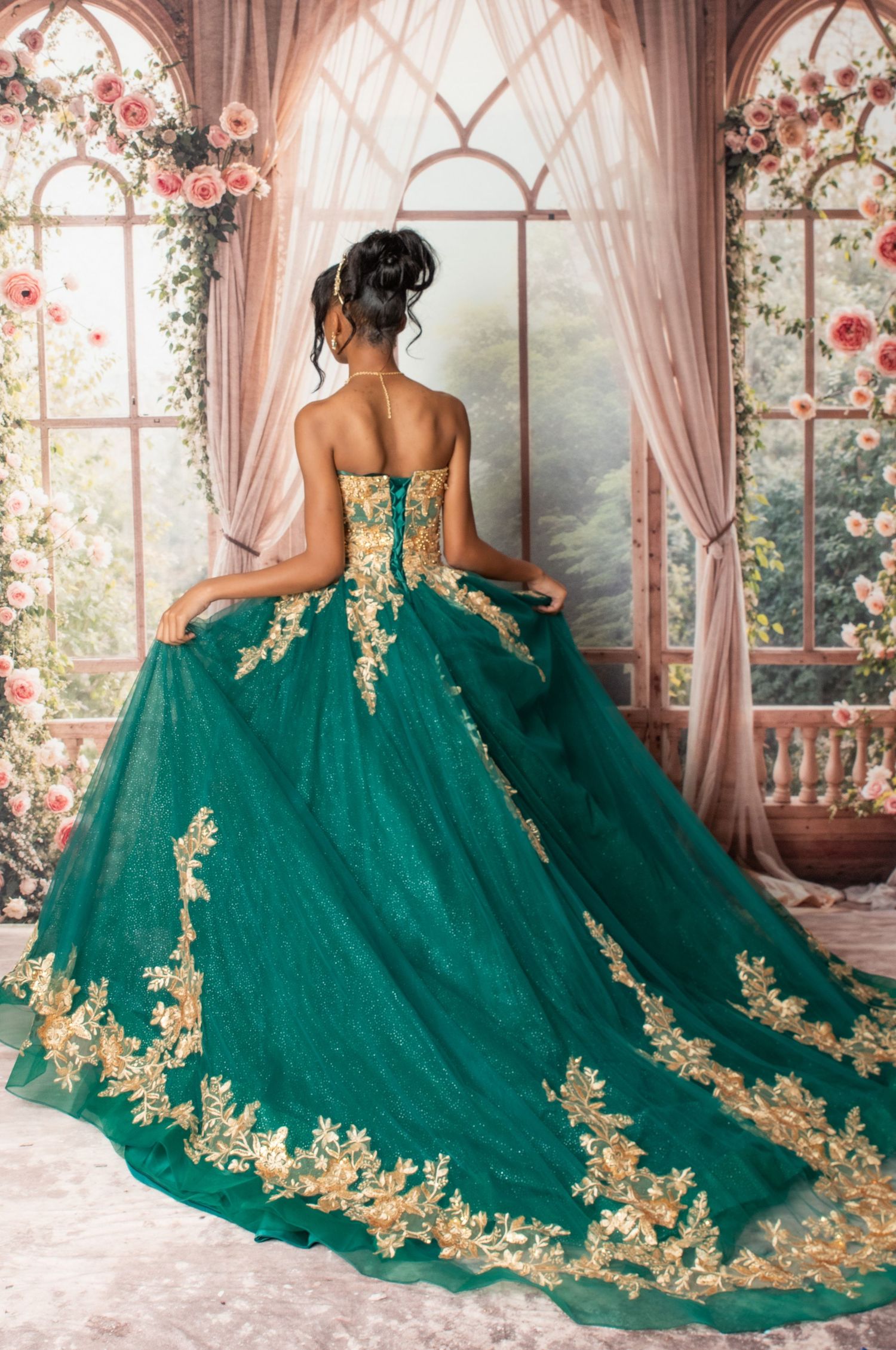 A stunning emerald green ball gown with gold lace appliques is showcased in an ornate conservatory with floral decor.
