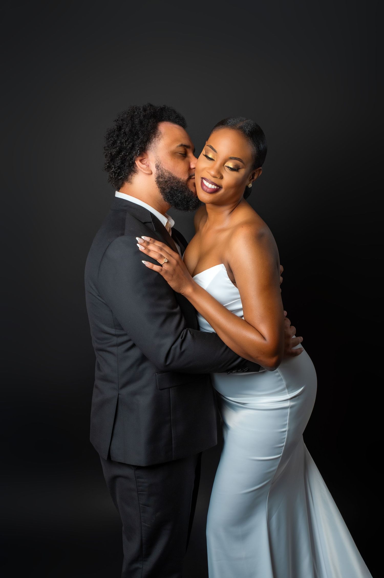 A romantic couple shares tender moments in an elegant portrait series against a dark backdrop with the person in white glowing.