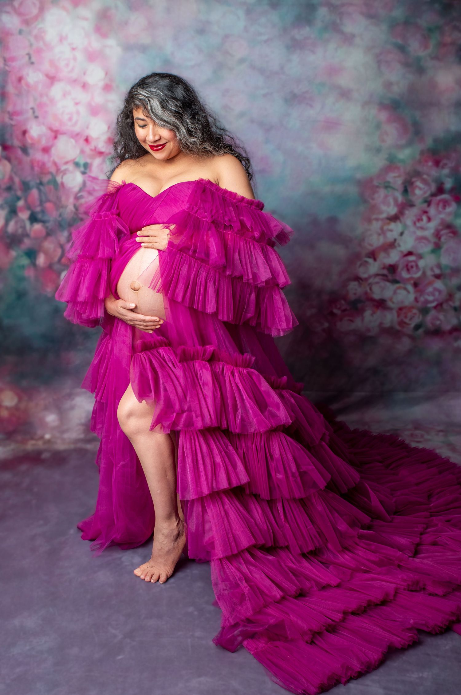A flowing magenta tulle gown with dramatic ruffled tiers creates an ethereal effect against a moody floral backdrop.