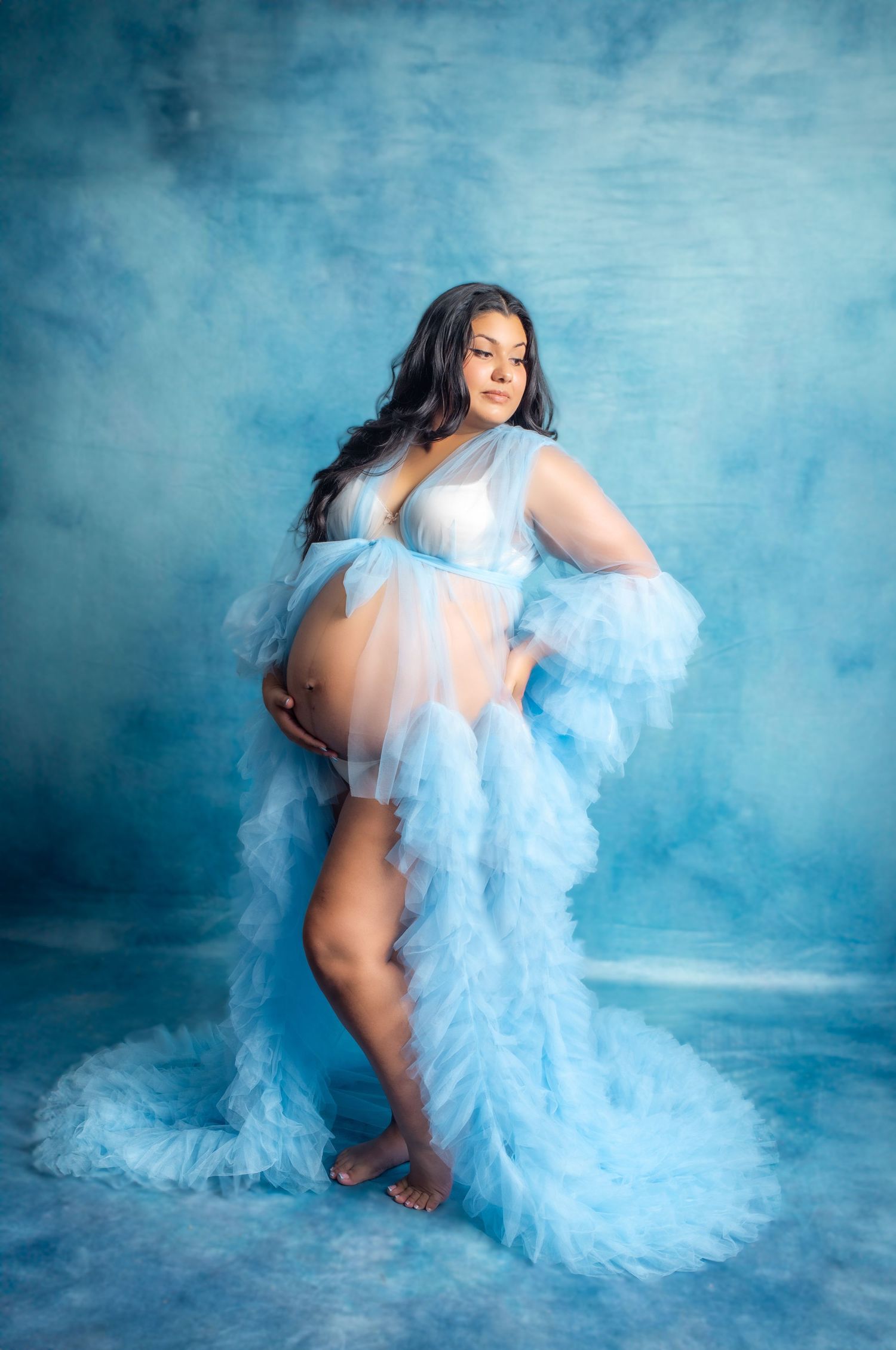 Artistic boudoir photo series with flowing light blue tulle fabric against misty blue studio backdrop creating ethereal effect.
