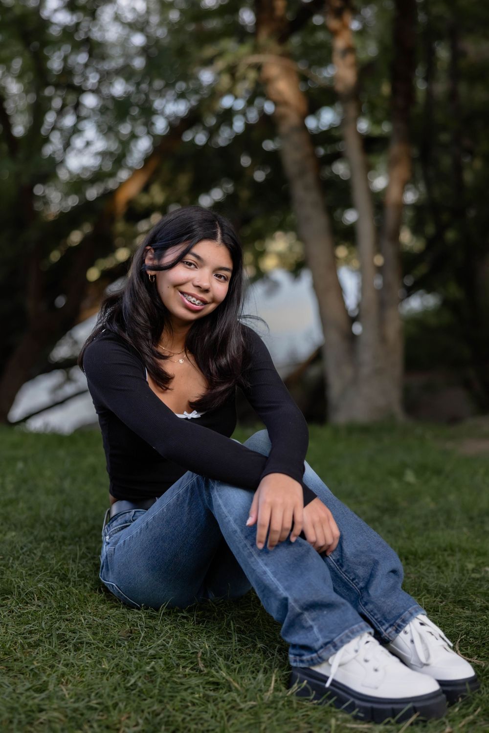 Person in casual outfit relaxing on grassy hill under trees.