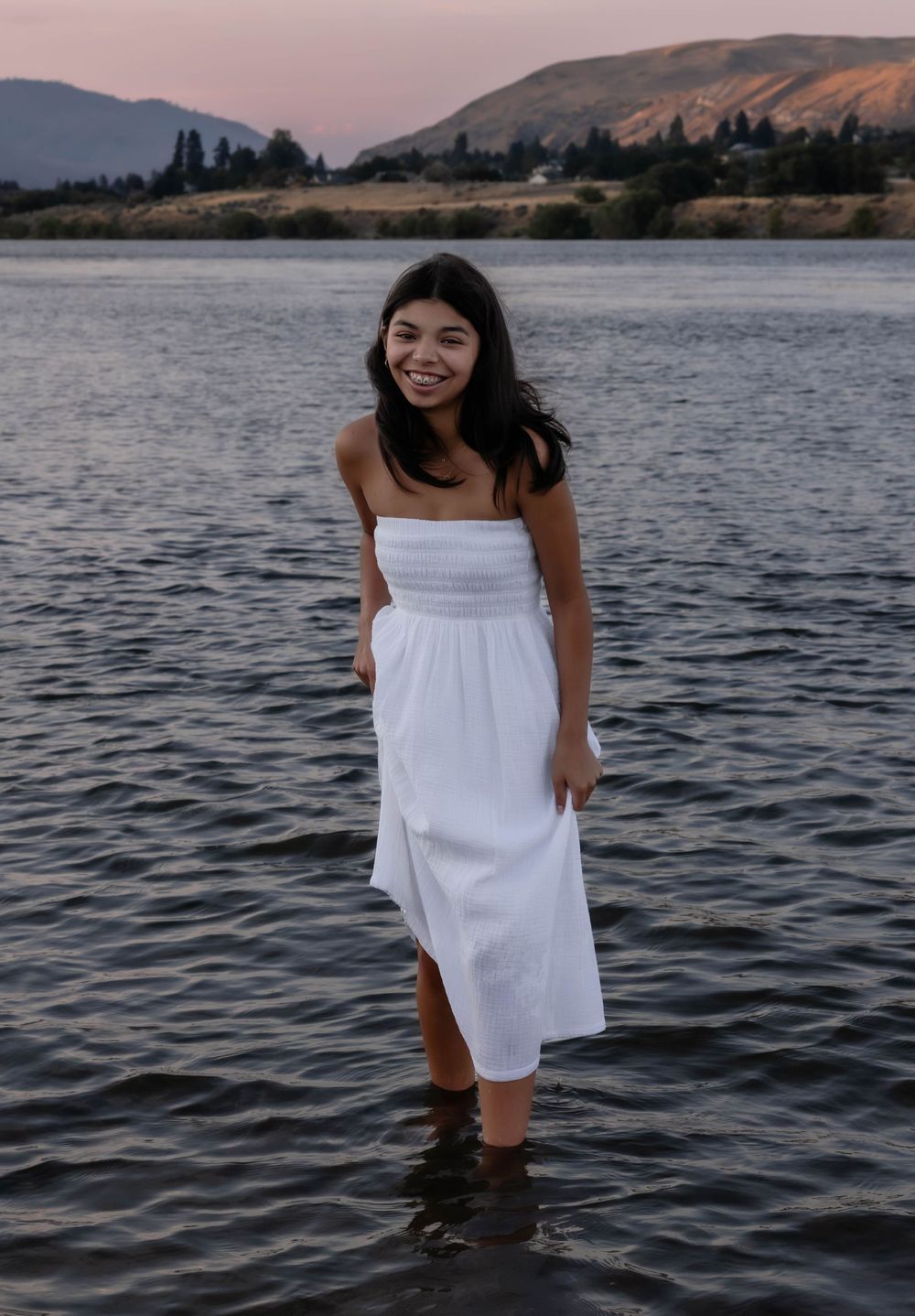Person wearing white dress plays in lake water during sunset.