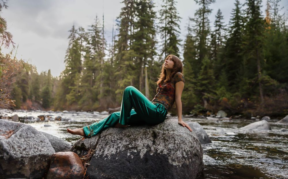 Dramatic poses on rocky riverbank with rushing water and evergreen forest.