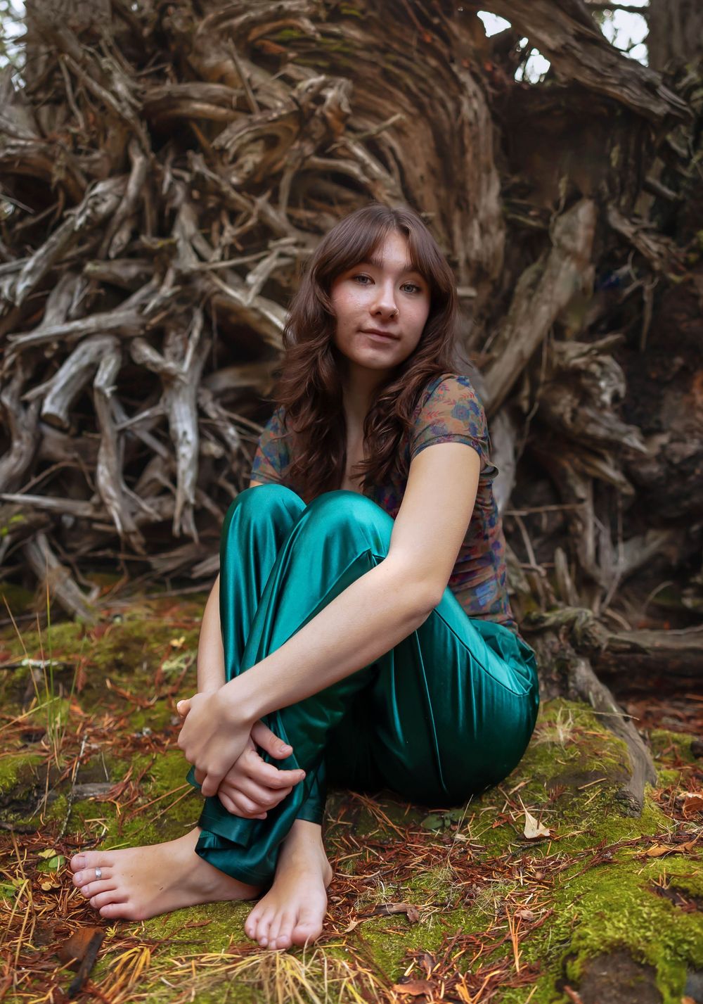 Artistic portrait among tree roots and moss wearing a teal dress in a forest setting.