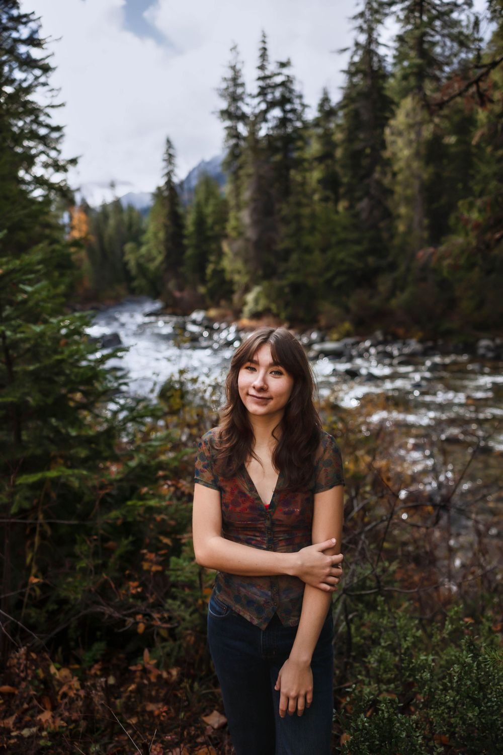 Outdoor portrait with snow-capped mountains and evergreen forest creating a dramatic backdrop.