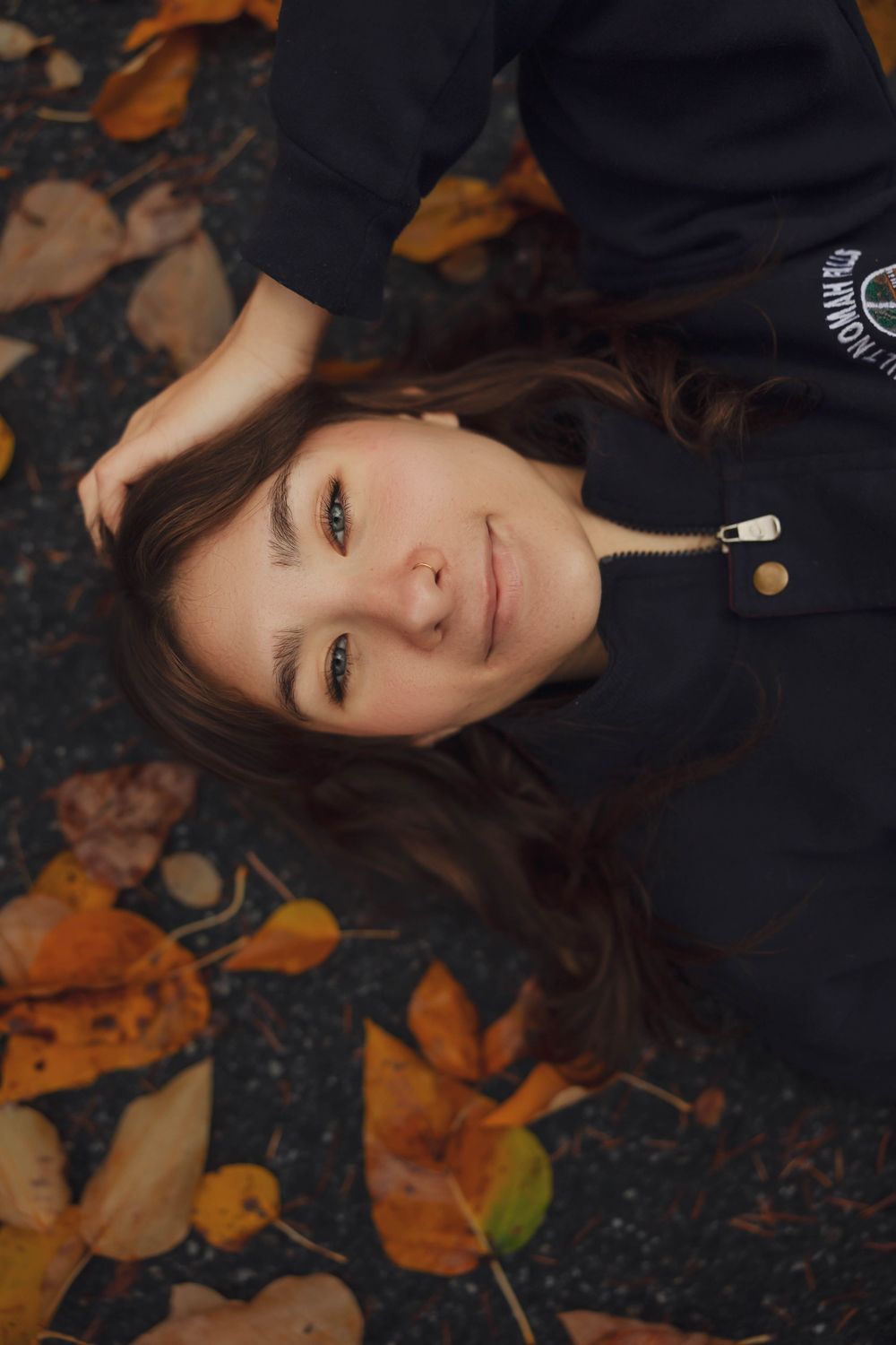 Artistic autumn portrait with orange fallen leaves creating a natural frame against dark background.