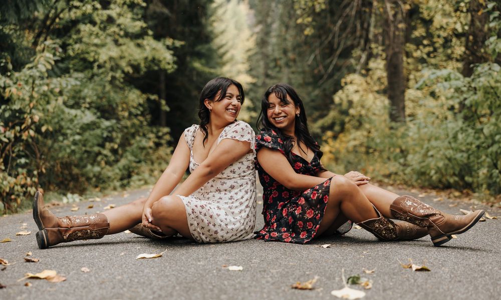 Friends in floral dresses relax on a forest path surrounded by autumn foliage.