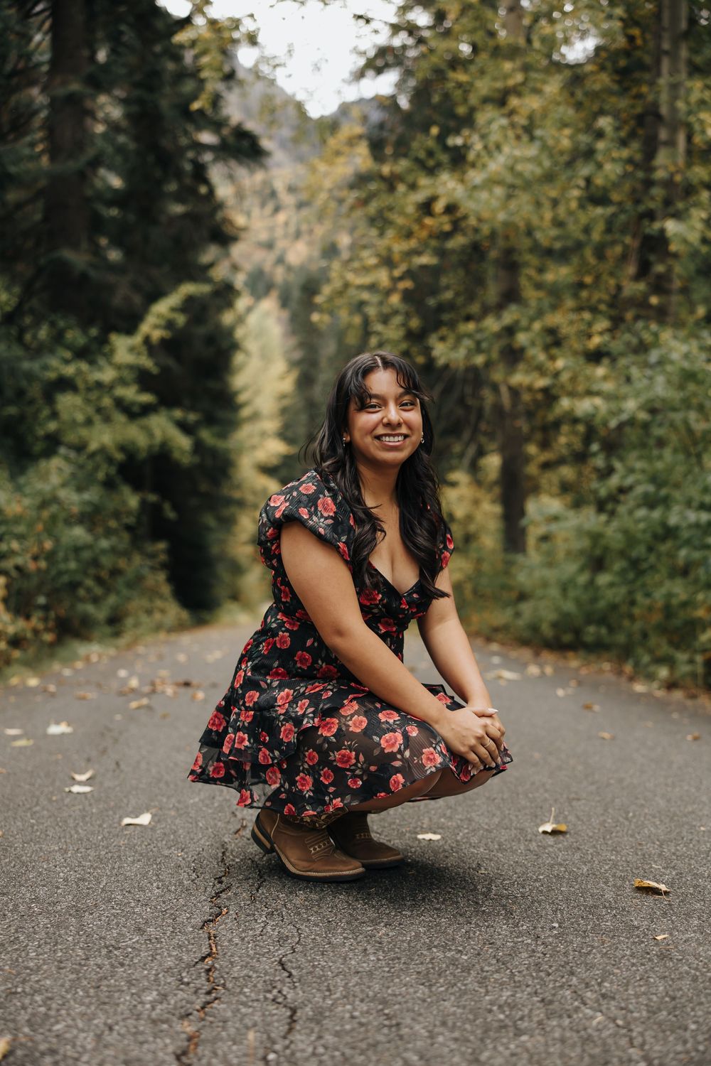Person in a red floral dress crouches on a forest path surrounded by autumn trees.