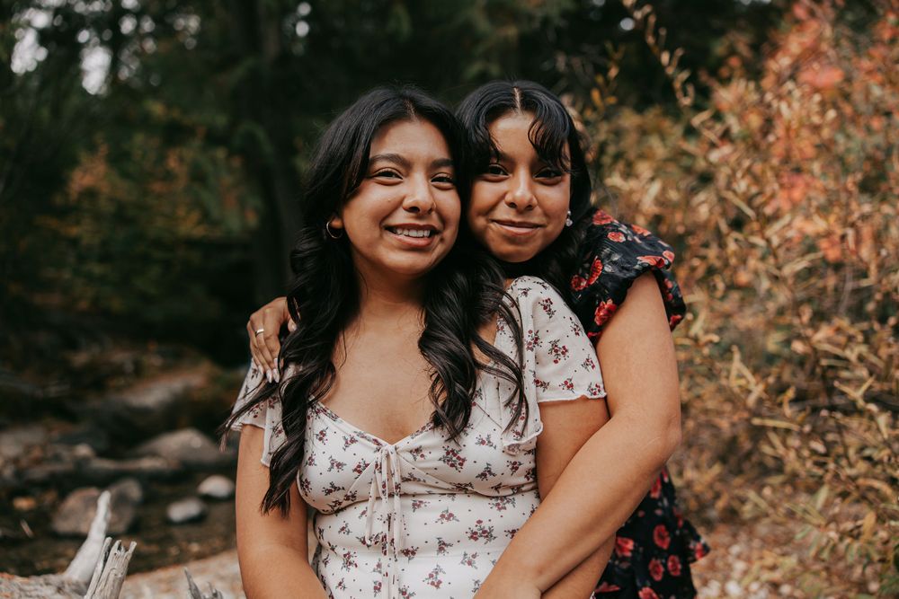 Two people in floral dresses embrace outdoors during an autumn photoshoot with warm lighting.
