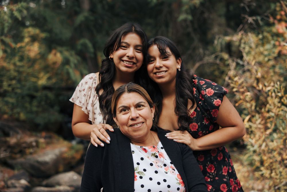Three people pose together for a family portrait outdoors with autumn foliage in the background.