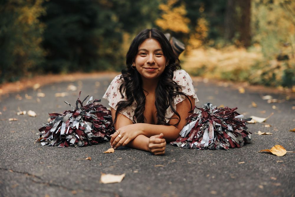 Person lying on forest path with pom poms during autumn photoshoot.