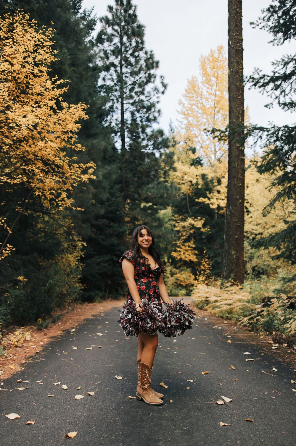 Person in floral dress poses on forest path surrounded by golden autumn trees.