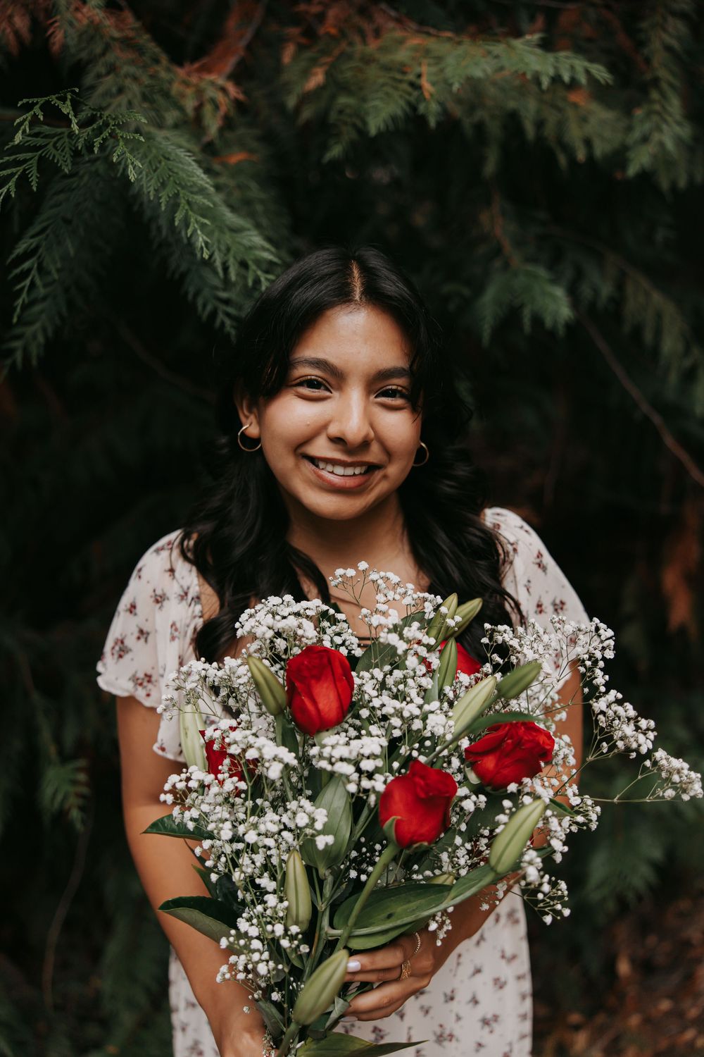A bouquet of red roses and baby's breath flowers held against a dark forest background.