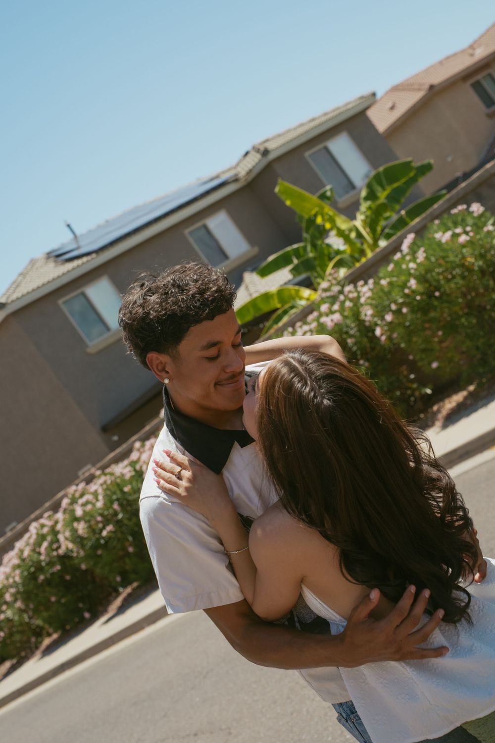 Young couple sharing a romantic embrace and kiss outdoors near a suburban home on a sunny day.