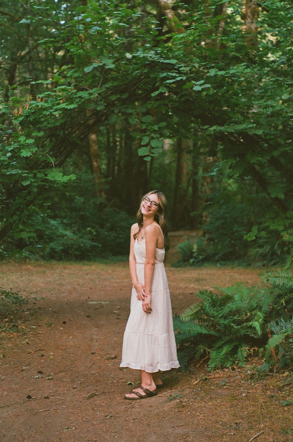 A person in a white lace dress twirls playfully in a wooded forest setting.