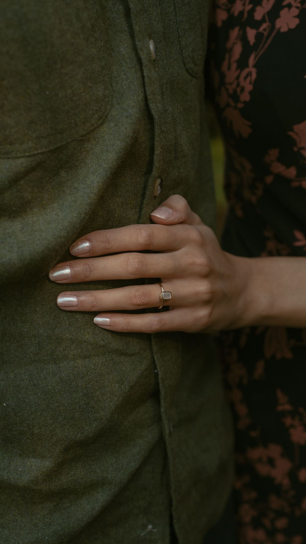 Close-up of a woman's hand with an engagement ring resting on a man's olive green shirt.