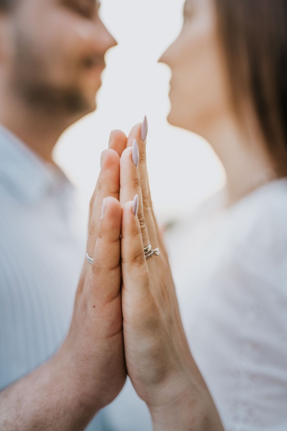 Close-up of two hands with an engagement ring touching in golden sunlight.