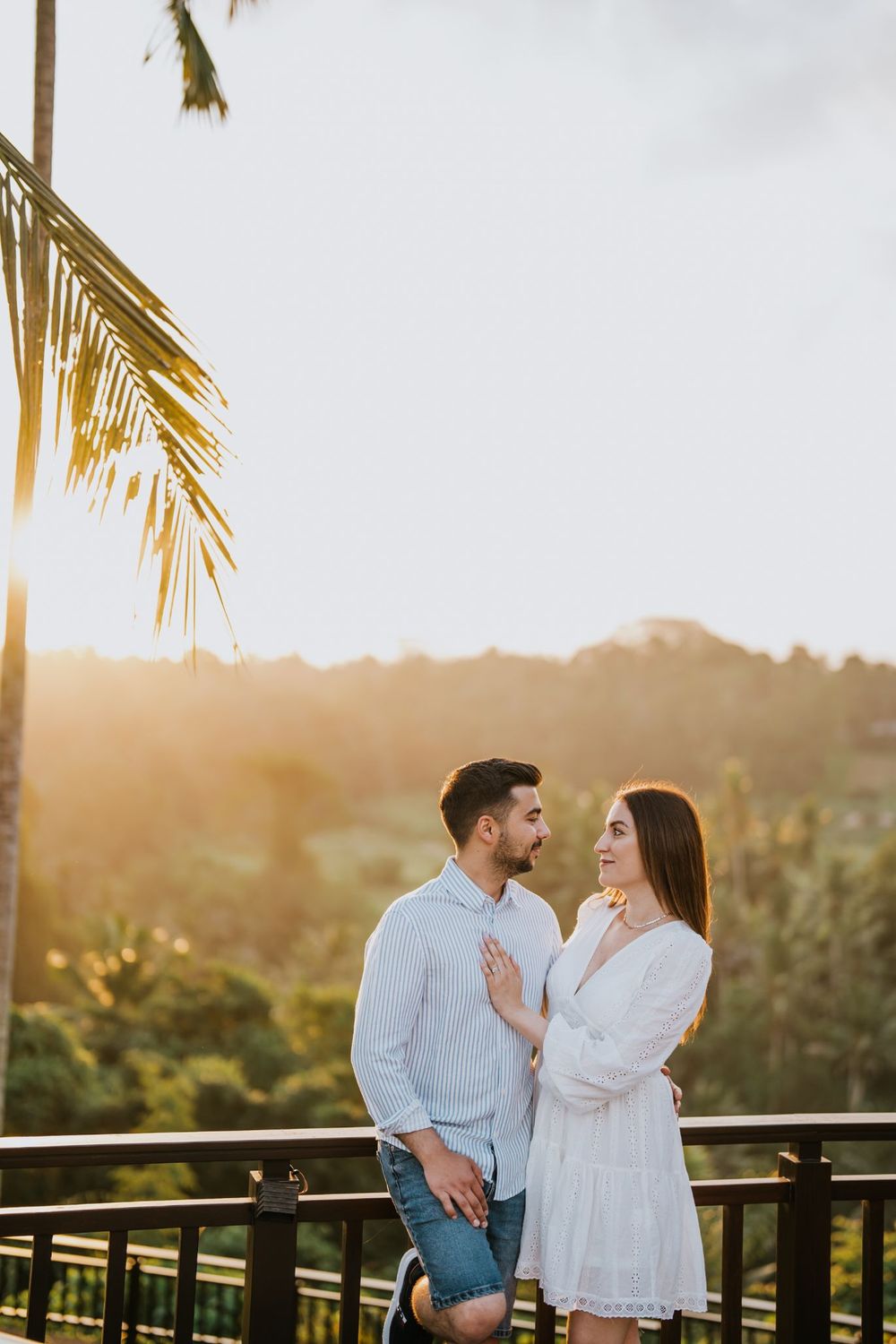 Couple enjoys sunset moment on tropical balcony with palm trees.